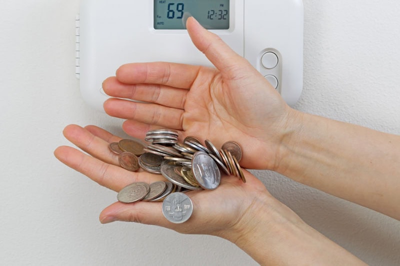 Homeowner holding tons of change near thermostat to represent saving money on your AC.